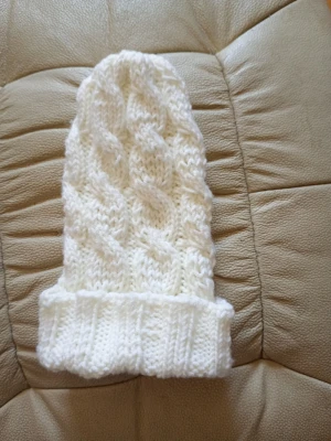 Hand-Knitted White Cable Beanie - These images show a hand-knitted white beanie hat with a cable knit pattern. The hat features a folded brim and a textured cable design running vertically. The yarn appears to be soft and thick, suitable for warmth in cold weather. Går att fås med eller utan tofs och meddela isåfall vad som önskas.