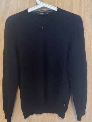 Svart V-ringad tröja från Boss - Klassisk svart tröja från Boss med V-ringning och långa ärmar. Tillverkad i ett mjukt och tunt material som passar perfekt till lager på lager. Enkel och stilren design utan mönster eller tryck.