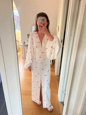 Vit långklänning med blommigt mönster - Vit långklänning från Adoore! Klänningen har knappar framtill och en slits nedtill. Tillverkad i ett strukturerat tyg som ger en lyxig känsla. Perfekt för sommaren😍🌸