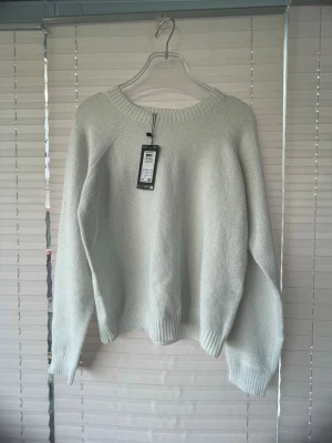 Vit stickad tröja från Vero Moda - Säljer en enkel och stilren vit stickad tröja från Vero Moda. Tröjan har rund halsringning, långa ärmar och ribbade muddar vid ärmslut och nederkant. Perfekt att matcha med jeans eller kjol för en clean look.