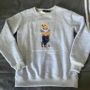 Grå sweatshirt Polo Bear Ralph Lauren - Grå  Ralph Lauren sweatshirt med ikoniska Polo Bear-trycket framtill. Mjuk bomullsmix och avslappnad passform. Perfekt för en casual och trendig look. ⁉️Skriv vid frågor⁉️