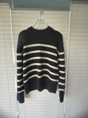 Svartvit randig stickad tröja Gina Tricot - Stickad tröja från Gina Tricot i svart med vita horisontella ränder. Tröjan har rund halsringning, långa ärmar och ribbade muddar vid ärmslut och nederkant. Perfekt för dig som gillar klassisk och enkel stil.