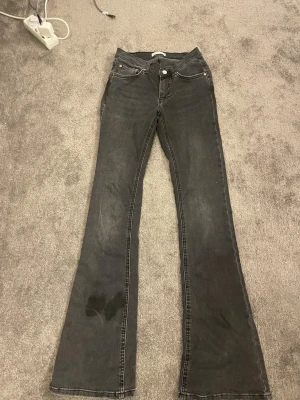 Grå bootcut jeans med slitningar - Säljer ett par grå bootcut jeans med lätt slitna detaljer och klassisk femficksmodell. Jeansen har utsvängda ben och synliga sömmar i kontrastfärg. Perfekta för dig som gillar en avslappnad men trendig look. Knappt använda.Fläcken är vatten som jag tagit för att få bort en fläck, de har torkat nu!