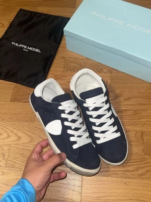 Philippe Model blåa sneakers - Snygga sneakers från Philippe Model i mörkblå mocka med vita detaljer och vita skosnören. Skorna har en klassisk låg siluett och vit sula. Perfekta för dig som vill ha en stilren och trendig look.