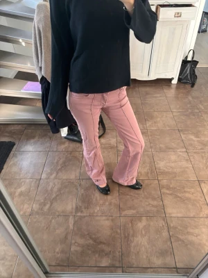 Rosa bootcut jeans med normalhög midja  - Säljer ett par rosa bootcut jeans med medelhög midja från bershka. Jeansen har klassisk femficksdesign och stängs med 2 knappar och dragkedja. Jeansen är lite stretchiga. Passar bra i längden på mig som är 170 cm. Har blivit lite slitna längst ner på ena benet som man ser på en av bilderna 