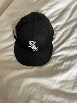 Svart Chicago White Sox keps - Säljer en svart keps med Chicago White Sox-logga broderad i vitt framtill och World Series-märke på sidan. Klassisk rak skärm och New Era-detalj på sidan. Perfekt för dig som gillar sportig streetstyle.