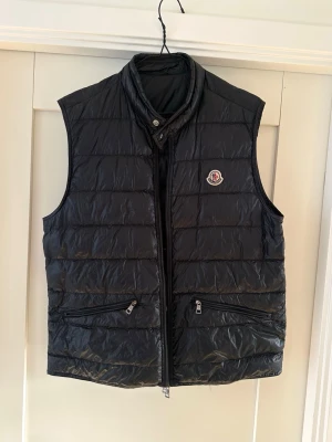 Moncler Gui väst L/XL - Säljer en marinblå Moncler gui väst i storlek 4 (L/XL).  Nypris: 9 315kr  Hängena på dragkedjorna har svag kromfärg (se bild) men utöver det är västen i mycket fint skick!  Äkthet garanteras. Originaletikett med QR kod finns kvar i västen. 