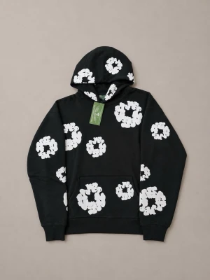 Denim Tears Cotton Wreath - Svart hoodie från Denim Tears med stora vita blommönster över hela tröjan. Klassisk huva och känguruficka framtill. Perfekt för dig som vill sticka ut med en cool och unik stil.