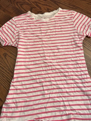 Vit och rosa randig t-shirt - Säljer en vit t-shirt med rosa horisontella ränder. Klassisk rund halsringning och korta ärmar.