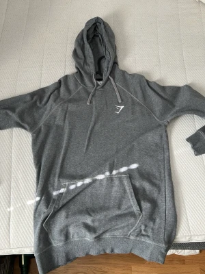 Grå hoodie från Gymshark I Medium - Säljer en grå hoodie från Gymshark med huva och dragsnören. Hoodien har en stor magficka och Gymshark-loggan broderad på bröstet. Perfekt för chill dagar eller träning. Mjuk och skön bomullsblandning.
