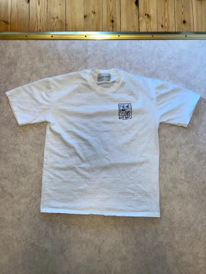 Vit t-shirt med tryck 'Cozy Day' - Vit t-shirt i bomull med svart tryck fram och stort grafiskt tryck på ryggen med texten 'Cozy Day :) Playing Records'. Klassisk passform och rund hals. Perfekt för dig som gillar enkel men cool stil.