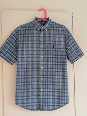 Polo Ralph Lauren kortärmad rutig skjorta 🐎 - Klassisk kortärmad skjorta från Polo Ralph Lauren i blå och grå toner. Rutig design, button-down-krage och broderad Ralph Lauren-logga på bröstet. Perfekt till sommaren och enkel att matcha med jeans, shorts eller chinos. Storlek: M Skick: Fint skick men den har nån defekt! Skriv gärna vid frågor eller om du vill ha mått!