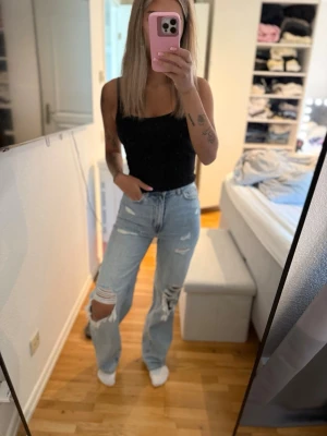 Ljusblå ripped straight leg jeans - Säljer ett par ljusblå jeans med raka ben och stora slitningar vid knäna. Jeansen har hög midja och klassisk femficksdesign. Perfekta för en avslappnad och trendig look. Materialet är denim i bomull.