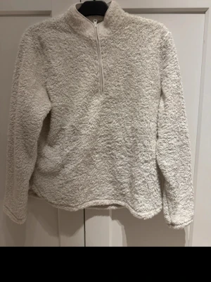 Vit fluffig fleece tröja med dragkedja - En supermjuk och fluffig vit fleece tröja med halv dragkedja framtill och hög krage. Långärmad modell i mysigt material som håller dig varm och bekväm. Perfekt för kyliga dagar när du vill ha något både stilrent och cozy.