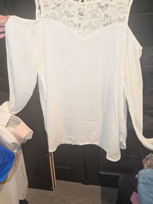 Vit blus från Guess med spetsdetaljer - Snygg vit blusnfrpn guess med långa ärmar och axelbandsmodell. Överdelen har vackra spetsdetaljer med blommönster och resten av blusen är i ett tunt, mjukt tyg. Har små fläckar under armarna 