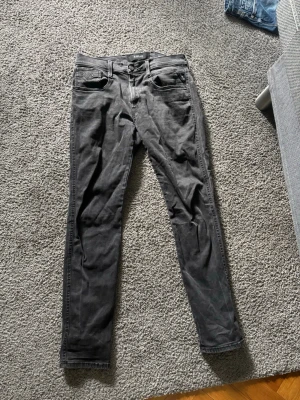 Svarta slim fit jeans från Replay - Säljer ett par svarta slim fit jeans från Replay, modell Anbass. Jeansen har klassisk femficksdesign, dragkedjegylf och är tillverkade i stretchigt denimtyg för extra komfort. Perfekta för en snygg och avslappnad stil.