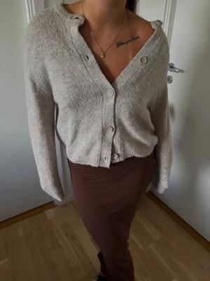 Beige stickad kofta med knappar - Mysig beige stickad kofta och knappar framtill. Koftan har lång ärm och en avslappnad passform
