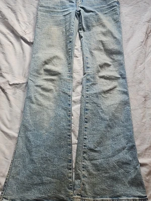 Ljusblåa utsvängda jeans - Säljer ett par ljusblå jeans med riktigt breda utsvängda ben. Jeansen har klassisk femficksdesign och snygga broderade detaljer på bakfickorna. Tillverkade i denim med en cool vintagekänsla. Perfekta för dig som gillar retrostil och vill sticka ut.