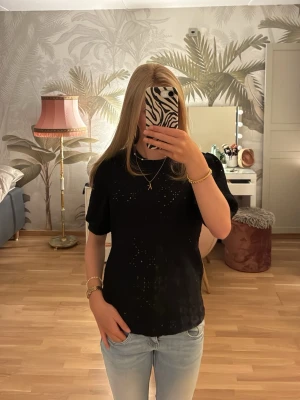 Svart topp med puffärm och hålmönster - Snygg svart topp med korta puffärmar och diskret hålmönster över hela tyget. Toppen har en rak passform och rund halsringning, perfekt att styla med jeans eller kjol. 