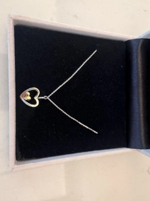 Halsband med hjärthänge från Guldfynd - Snyggt halsband i silverfärg från Guldfynd med ett öppet hjärthänge. Inuti det större hjärtat finns ett mindre hjärta i guldton, vilket ger en fin kontrast. Nypris ca 300kr.  Aldrig använt så i helt nyskick. Meddela för frågor, skickar snabbt:)