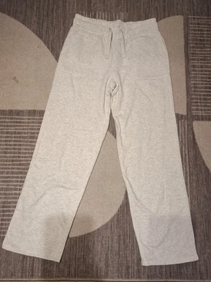 Ljusgrå mjukisbyxor med raka ben - Ljusgrå mjukisbyxor med raka ben och resår i midjan samt dragsko. Byxorna har fickor fram och bak, och är tillverkade i ett mjukt och bekvämt material som passar perfekt för chill dagar. Enkel och stilren design som funkar till det mesta.