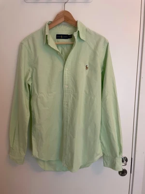 Ljusgrön skjorta från Ralph Lauren - Snygg ljusgrön skjorta från Ralph Lauren med klassisk krage och broderad logga på bröstet. Skjortan har knäppning framtill och är tillverkad i ett mjukt bomullstyg. Perfekt för en clean och stilren look. Pris kan givetvis diskuteras. 