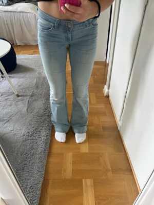 Ljusblå bootcut jeans - Säljer ett par ljusblå bootcut jeans med klassisk femficksdesign och broderade detaljer på bakfickorna. Jeansen har normal midja och är tillverkade i ett mjukt denimtyg som sitter bekvämt. Perfekta för en avslappnad och trendig look.