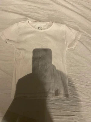 Vit ribbad t-shirt från 157 - En basic vit ribbad t-shirt från 157 med rund hals och korta ärmar. Tillverkad i mjuk bomull med lite stretch för extra komfort. Perfekt att matcha med jeans eller kjol för en clean och enkel look.