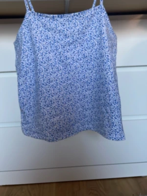 Blommig blå och vit linnetopp - Söt linnetopp med tunna axelband och småblommigt mönster i blått och vitt. Perfekt för varma dagar och enkel att matcha med jeans eller kjol. Lätt och luftig känsla.
