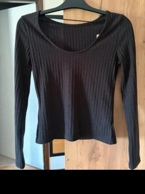 Svart ribbad långärmad topp - Säljer en svart ribbad långärmad topp med rund halsringning. Toppen har en slim passform och är tillverkad i ett mjukt, stretchigt material som sitter snyggt på kroppen. Perfekt att styla med jeans eller kjol.