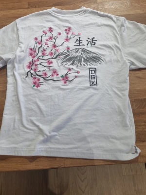 T shirt med design - Vit t-shirt från DGK med snygg baksida, backsidan är broderad och i mycket hög kvalite. stor i storlekn, storlek s,  #baggyjeans #lowwaist jeans #cargobyxor #vida jeans #flarejeans #lågmidja #rakajeans #kostymbyxor #mjukisbyxor #oversizedhoodie #ziphoodie #stickadtröja #corsettopp #offshoulder #babytee #linne med spets #oversized tshirt #stickadväst #maxikjol #y2k #vintage #streetwear #oldmoney #cleangirl #basic #festkläder #vardagskläder #unisex #oversized #fitted #cozy #retro #zara #hm #bikbok