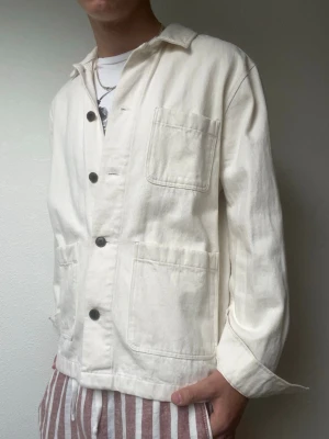 Offwhite overshirt - Strl M - Stilren overshirt i kraftigare bomull med workwear-inspirerad design och stora framfickor. Passar perfekt som vår- och höstjacka eller som ett extra lager.  • Mycket fint skick • Klassisk relaxed passform • Modellen på bilden är 178 cm / 70 kg.