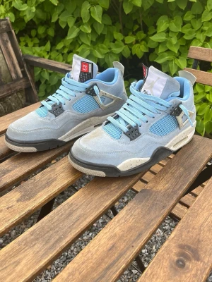 Blå och grå Air Jordan 4 sneakers - Snygga Air Jordan 4 sneakers i blått och grått med svarta och vita detaljer. Storlek 41, jag säljer dem för dem inte längre passar, mycket bra skick, fina och bra att ha nu till hösten närmar sig! Köpte dem för 1599kr säljer dem nu för 799kr mycket bra pris. Original kartong medges!