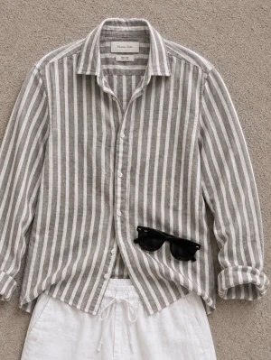 Randig linneskjorta från Massimo Dutti - Snygg randig skjorta från Massimo Dutti i 100% linne. Skjortan har en avslappnad passform, klassisk krage och knäppning framtill. Perfekt för varma dagar och ger en fräsch look med sina vita och grå ränder.