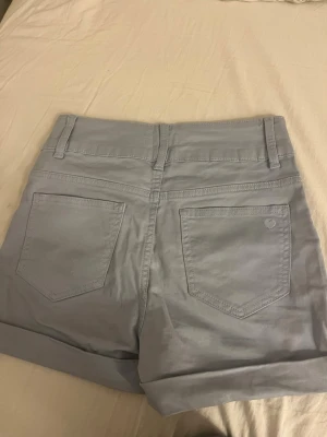 Ljusblå high-waist shorts med knappar - Säljer ett par ljusblå high-waist shorts med fyra silverfärgade knappar framtill. Storlek 152, fungerar som  xs
