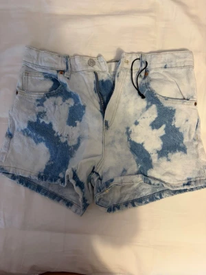 Tie dye shorts från Zara kids - Säljer ett par coola jeansshorts i storlek 13-14 med blekt batikmönster i blått och vitt. Shortsen har råa kanter, fem fickor och knappgylf. Perfekta för sommaren och ger en avslappnad vibe till din outfit.
