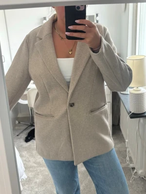 Beige oversized kavaj med knapp - Stilren beige kavaj i oversized modell med en knapp framtill och två fickor. Klassisk krage och mjukt material som ger en avslappnad men ändå snygg look. Perfekt att slänga över en topp och jeans för en trendig outfit.