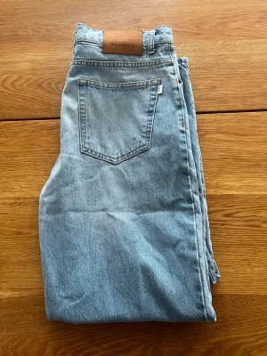 Ljusblå jeans från Woodbird - Säljer ett par ljusblå jeans från Woodbird. Jeansen har en avslappnad passform och är tillverkade i ett slitstarkt denimmatrial.