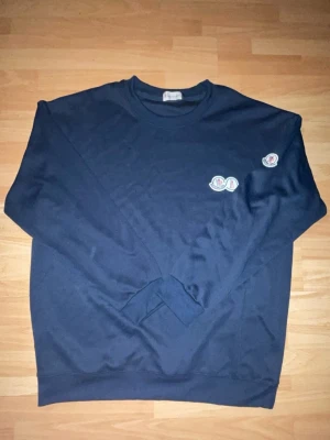 Mörkblå sweatshirt från Moncler - Mörkblå sweatshirt från Moncler med rund halsringning och logotyp-patch på bröstet samt ärmen. Tröjan har en avslappnad passform och är tillverkad i mjukt bomullsmaterial. Perfekt för en casual och stilren look.