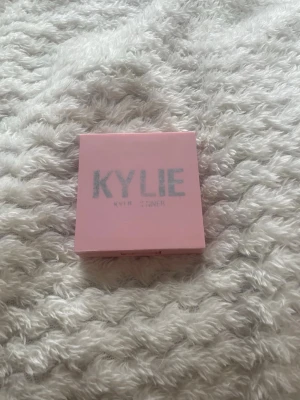 Kylie Cosmetics rosa puderrouge - Säljer ett puderrouge från Kylie Cosmetics i en söt rosa fyrkantig dosa med spegel. Rouget har en ljusrosa nyans som ger kinderna en fräsch och naturlig look. Perfekt för dig som gillar en mjuk och feminin touch till din makeup.