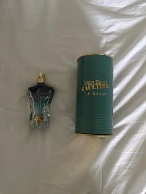 Jean Paul Gaultier Le Beau parfym - Säljer en Jean Paul Gaultier Le Beau parfym i en unik flaska formad som en manlig torso. Flaskan är genomskinlig med blågrön vätska och har gulddetaljer. Medföljer original grön metalltub med guldfärgad text. Perfekt för dig som gillar exklusiva dofter. Rätt mycket kvar 