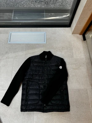 Moncler cardigan  - Svart Moncler cardigan som bara har används ett fåtal gånger. Jackan är storlek L dock så är den ganska så stor i storleken. Pris lappen på jackan är avklippt men den finns fortfarande kvar. Har du några frågor? Hör bara av dig!