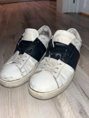 Valentino opens  - Snygga vita sneakers med bred svart läderdetalj över sidan och klassisk snörning. Skorna har en låg profil och en chunky sula med mönstrad häl. Perfekta för en stilren och trendig look. Syns på användning, priset inte hugget i sten 