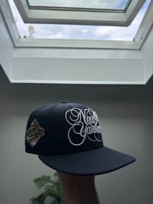 New York Yankees marin blå keps - Snygg blå keps med stor broderad New York Yankees-logga i vitt framtill. På sidan finns en patch med gulddetaljer och broderad text.       Säljer för att den var för liten för mig. Köpte från topperzstore för 549 kr. Aldrig använd.