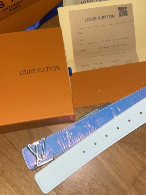 Louis Vuitton  - Säljer ett Louis Vuitton bälte med holografisk, skimrande yta och silverfärgat LV-spänne. Bältet har en vit insida och klassisk design som sticker ut med sin futuristiska look. Perfekt accessoar för dig som vill ha något unikt och trendigt.