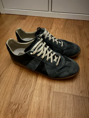 Mörkgrå sneakers med mockadetaljer - Snygga sneakers i mörkgrått med ovandel i mocka och läder, vita snören och klassisk gummisula. Skorna har en låg profil och stilren design som passar till många olika outfits.                  Låda finns ej!