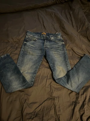 Blå Jack & Jones jeans 27/30 - Säljer ett par klassiska blå jack & Jones jeans snyggt tvättad look och raka ben. Jeansen har fem fickor, bälteshällor och stängs med knapp och dragkedja. Perfekta för dig som gillar en avslappnad men stilren stil.