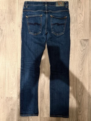 Nudie Jeans Grim Tim Dry Blå W32/L32 - Slim Straight Fit - Nudie Jeans Grim Tim ”Dry Open Navy” blåa jeans med slim straight fit-passform, normal midja och raka ben, storlek W32/L32, midja 37 cm, ytterbenslängd 98 cm, benöppning 16 cm, modellen är 185cm & väger 65kg, i fint skick.