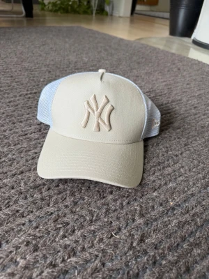 Beige New York Yankees keps - Snygg beige keps från New Era med broderad New York Yankees-logga framtill. Kepsen har böjd skärm och mesh-paneler i vitt på sidorna för extra ventilation. Perfekt för dig som gillar sportig och avslappnad stil.