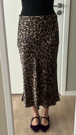 Leopardmönstrad långkjol i satin - Snygg långkjol med leopardmönster i bruna och svarta toner. Kjolen har en mjuk, glansig satinlook och sitter figurnära upptill med lätt utsvängd nederdel. Kjolen har tyvärr en defekt på höger sida (se bild)🤎🐆